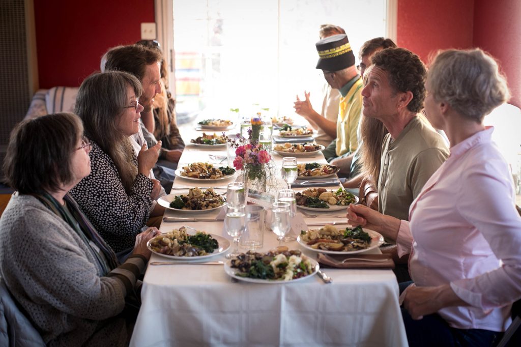 A group of Canticle Farm residents gather together for a vegetarian supper at a dinner table marked by bouquets of fresh flowers.
