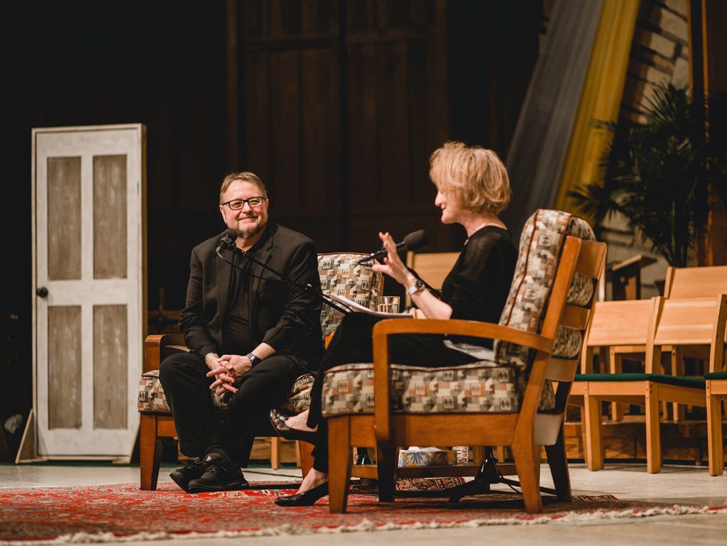 On Being host Krista Tippett interviews a man on stage at a live event.