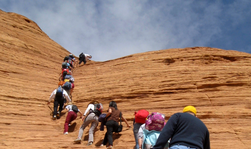 Young people and mentors hike in a line up a red rock hill in Arizona.