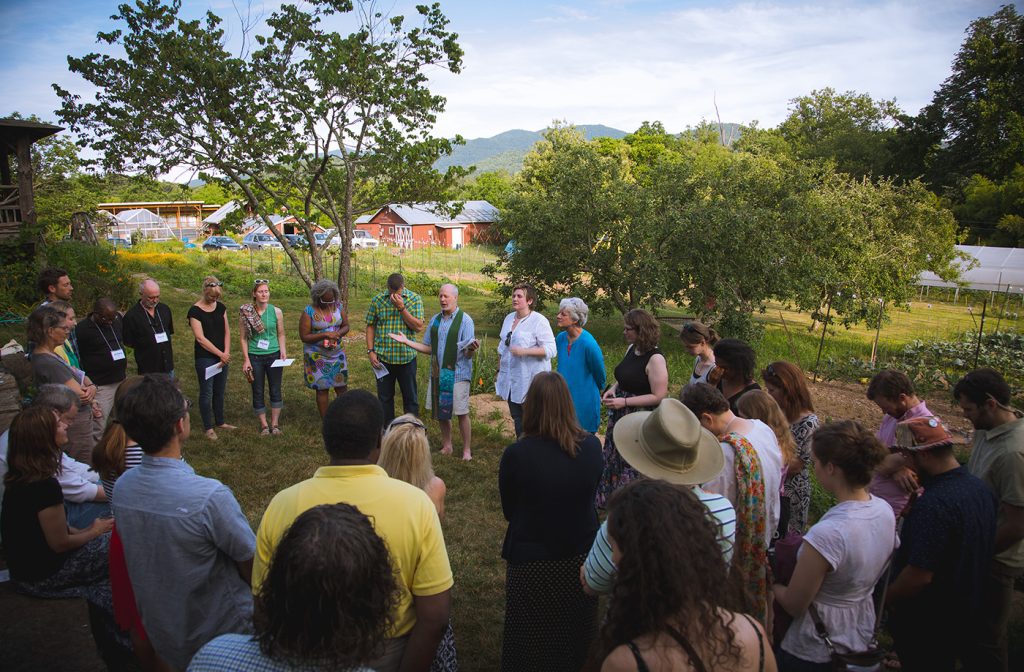 Students gather in a standing circle on a farm during the summer.