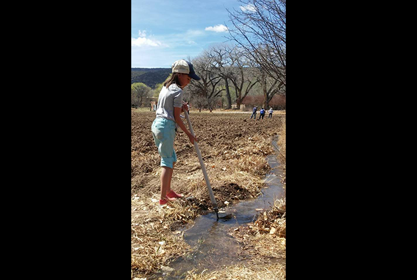 A girl works the acequia with a tool.