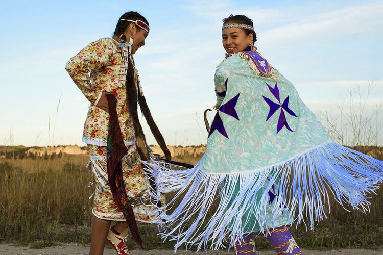 Two young women from the Pine Ridge Girls' School wearing regalia.
