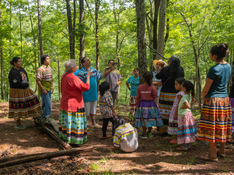 Native Maskoke people gathered in a circle in a forest.