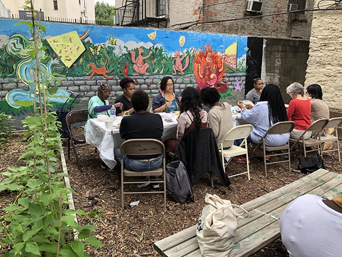 Participants at Kelly Street Garden sit around a table in the garden near a mural.